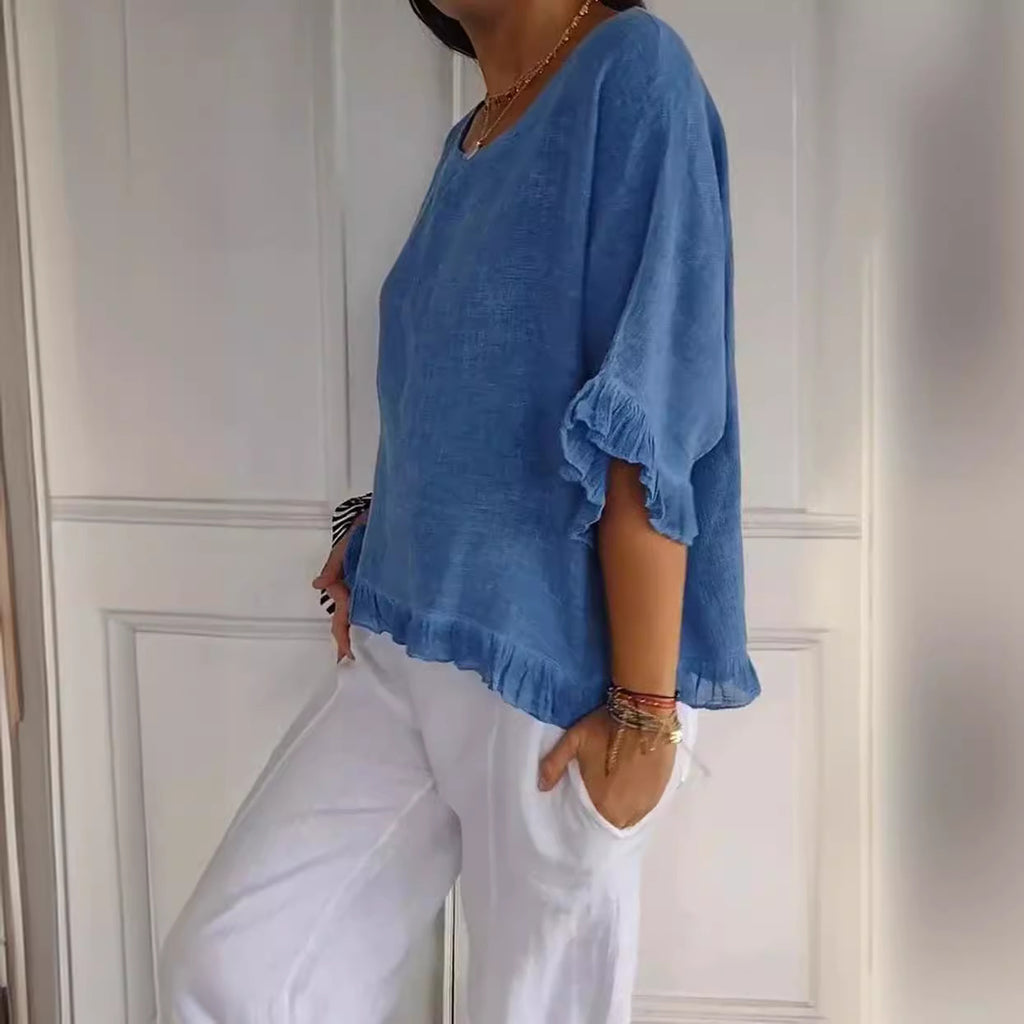 Person wearing a blue top and white pants against a white wall