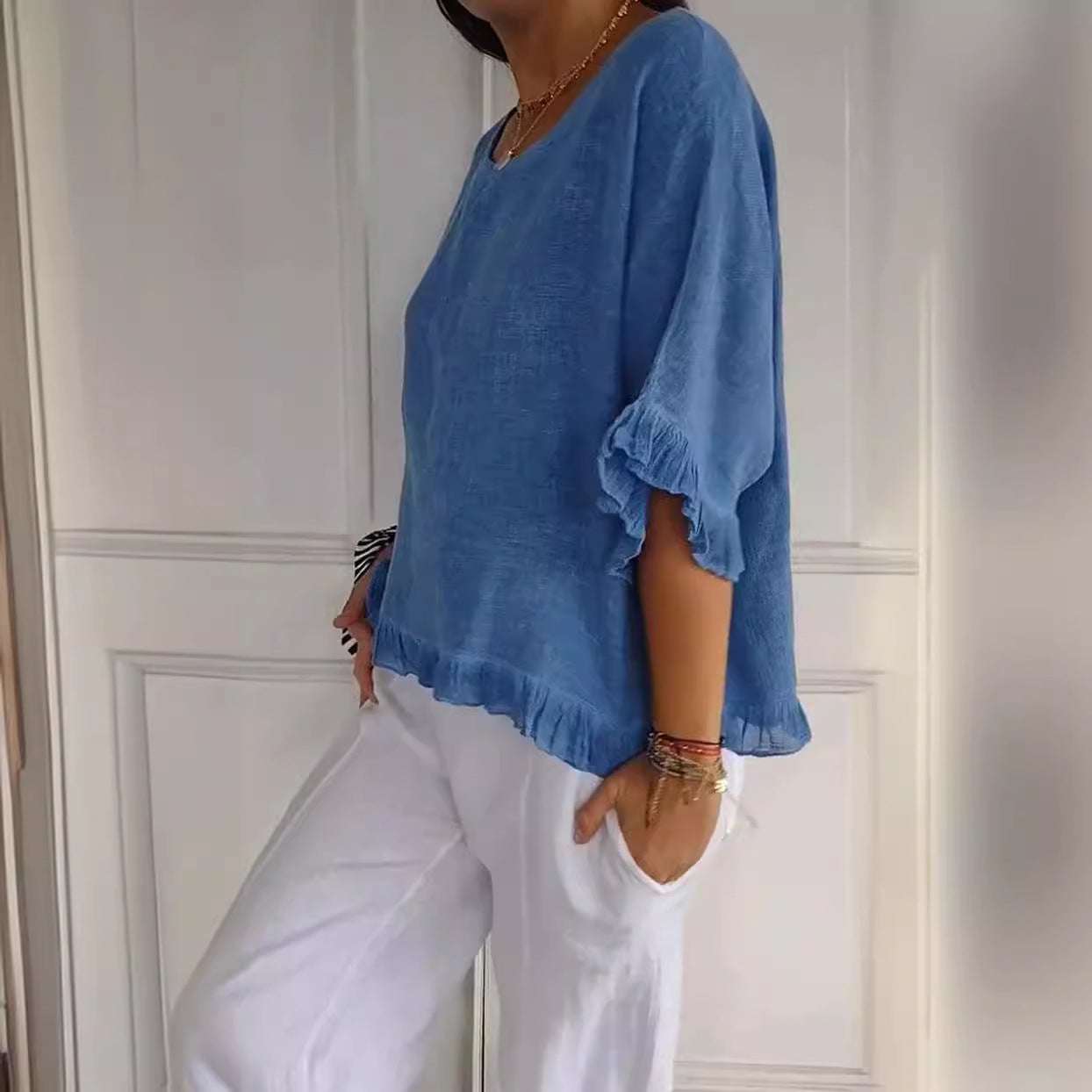 Person wearing a blue top and white pants against a white wall