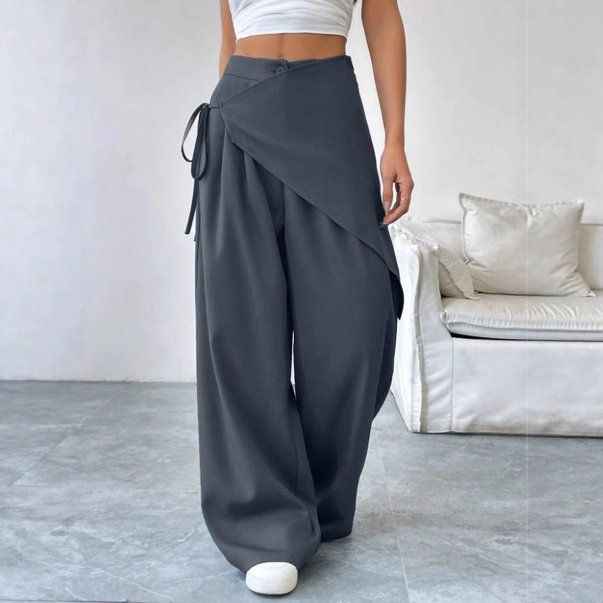Person wearing gray wide-leg pants in a minimalistic room with a sofa.