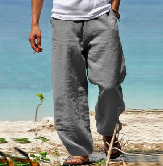 Person wearing gray pants standing on a beach with clear blue water in the background