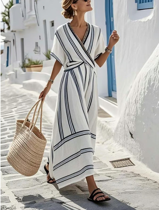 Woman in a white and blue striped dress holding a straw bag on a sunlit street.
