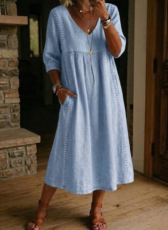 Woman wearing a light blue dress standing in a room with wooden flooring and a stone fireplace.