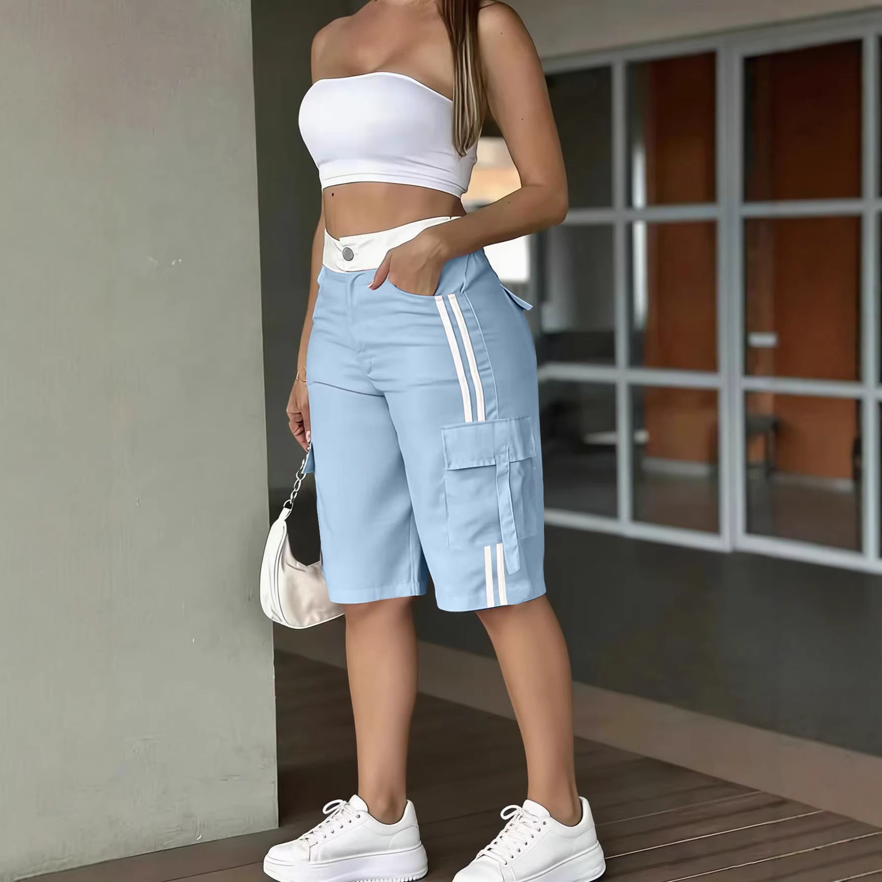 Person wearing a white crop top and light blue cargo shorts with white stripes, standing indoors.