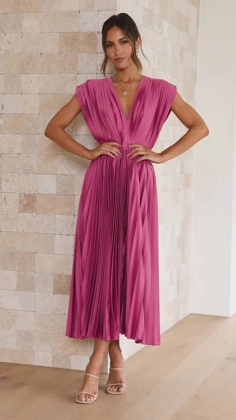 Woman wearing a pink pleated dress against a beige wall.