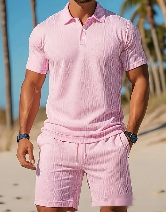 Person wearing a pink polo shirt and shorts set on a beach.