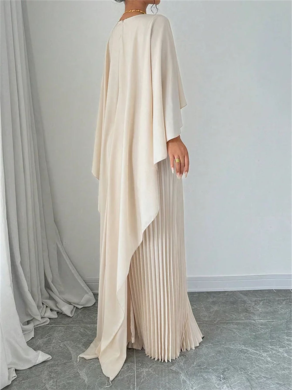 Woman wearing a long, light-colored dress with a pleated skirt against a plain background.