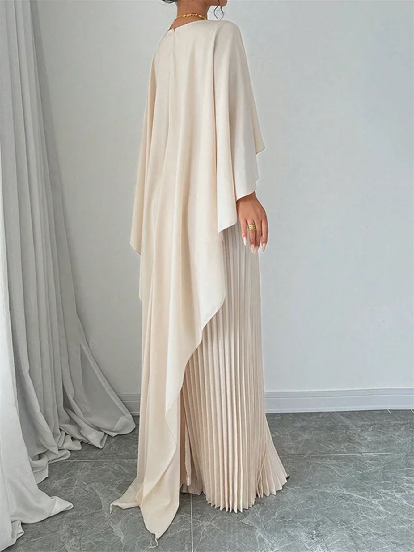Woman wearing a long, light-colored dress with a pleated skirt against a plain background.