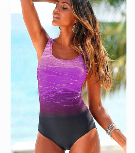Woman wearing a purple and black swimsuit with a blurred beach background
