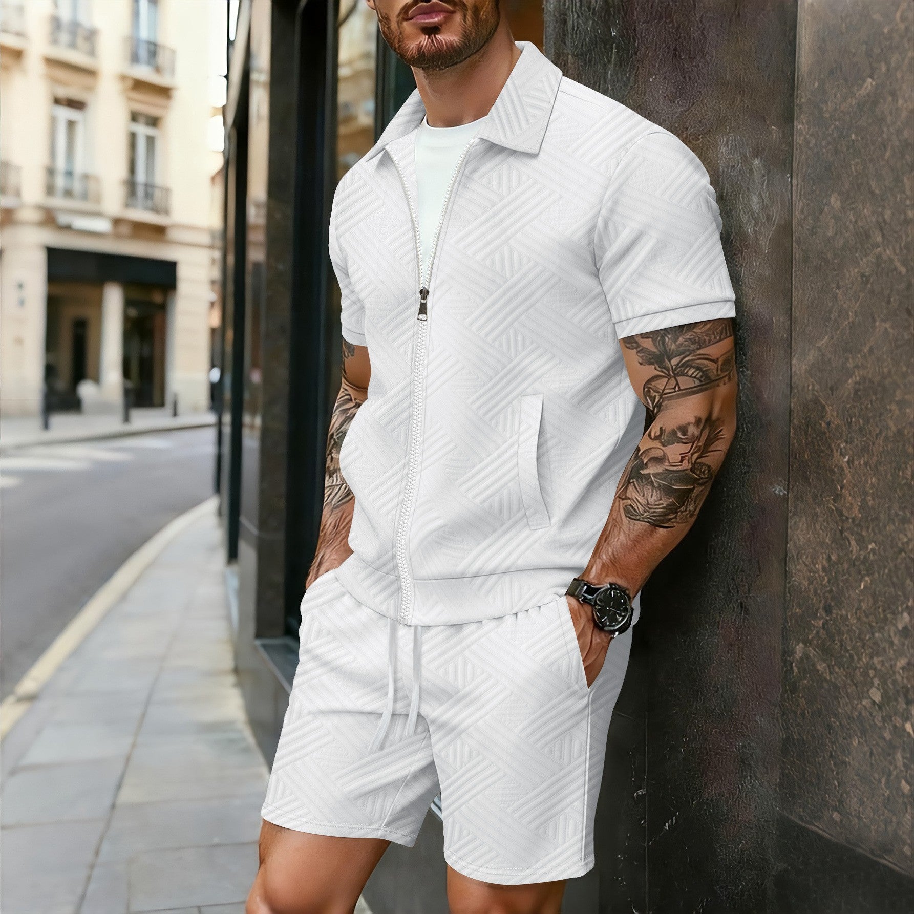 Man wearing a white textured outfit leaning against a wall on a city street.