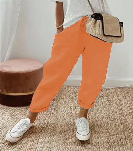 Person wearing orange pants and white sneakers with a beige bag indoors.