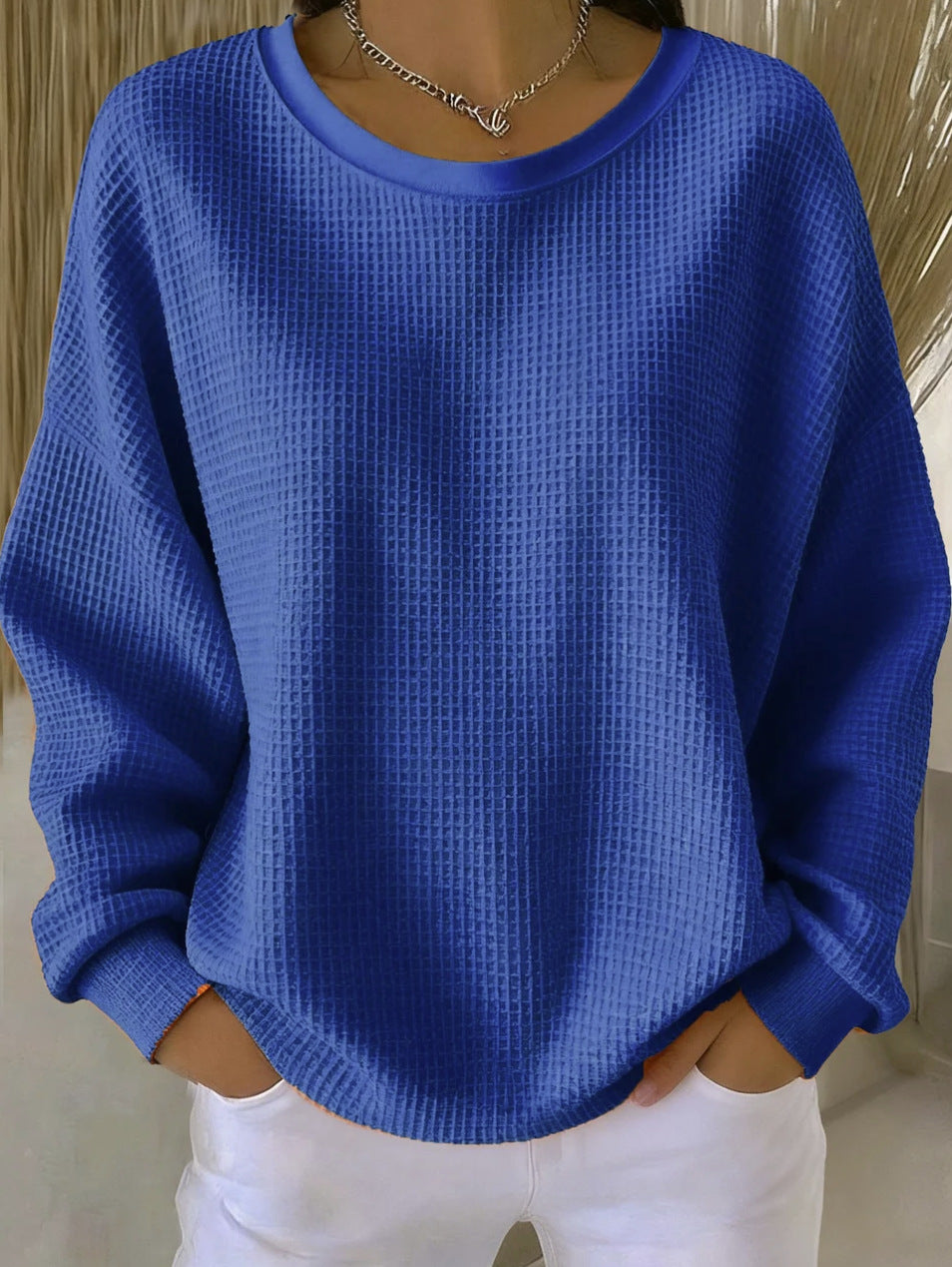 Person wearing a blue textured sweater with white pants against a neutral background