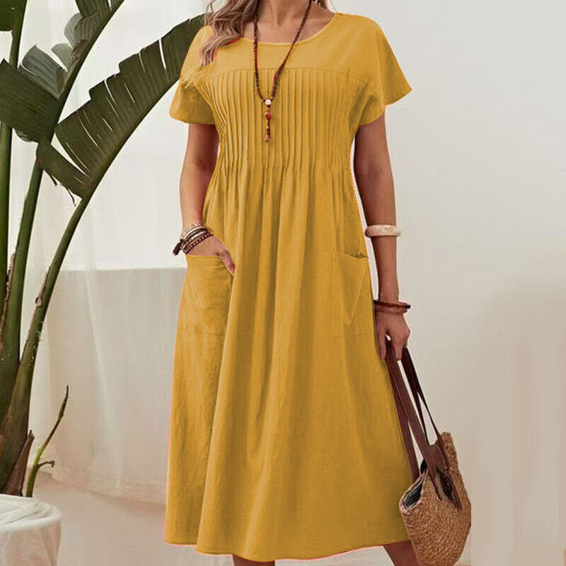 Woman wearing a yellow dress holding a straw bag indoors with a plant in the background