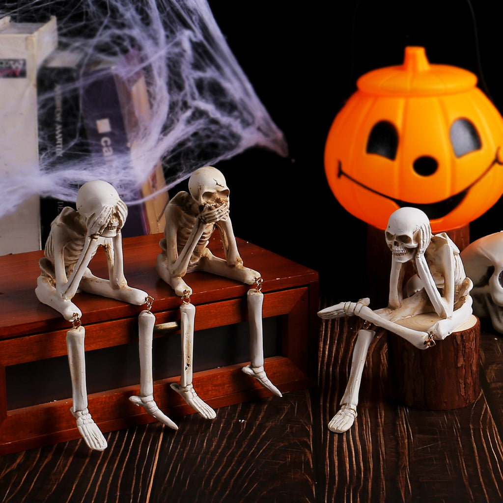 Three skeleton figurines with blindfold, ear, and mouth on a wooden surface with Halloween decorations.
