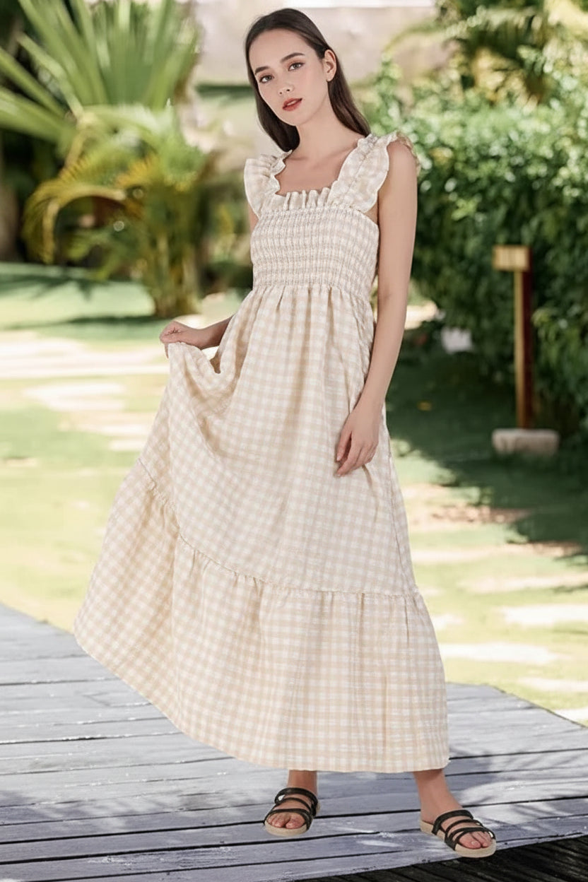 Woman in a long checkered dress standing on a wooden deck with greenery in the background