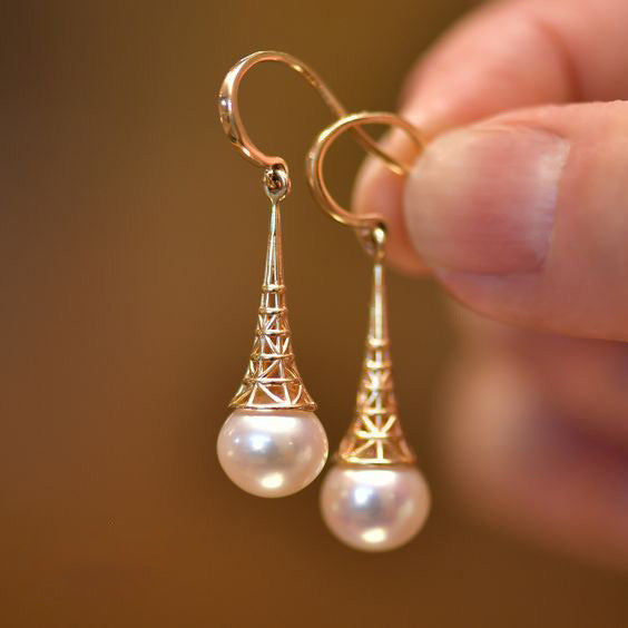 Gold earrings with pearl drops held by a hand against a blurred background