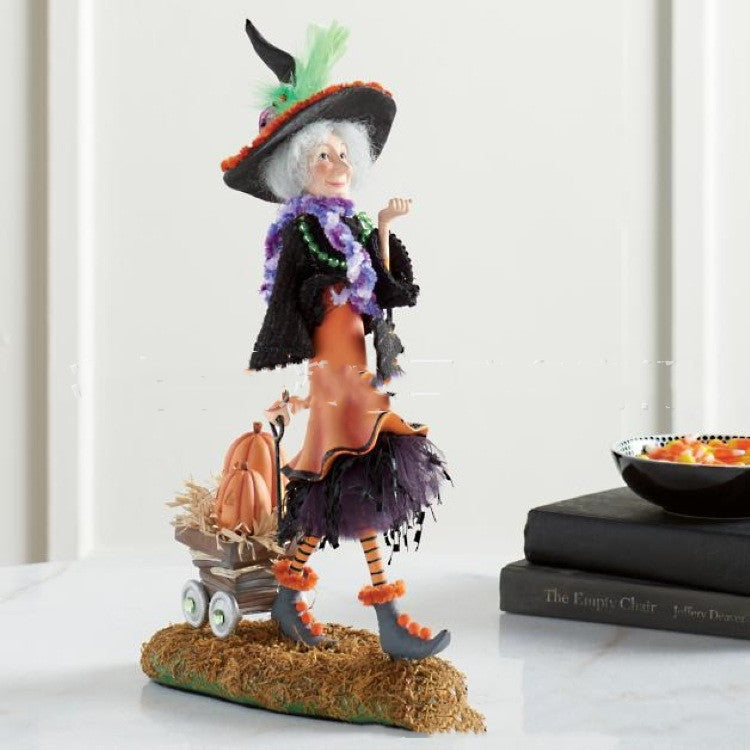 Halloween-themed figurine of a witch with a broom and pumpkin on a white surface.