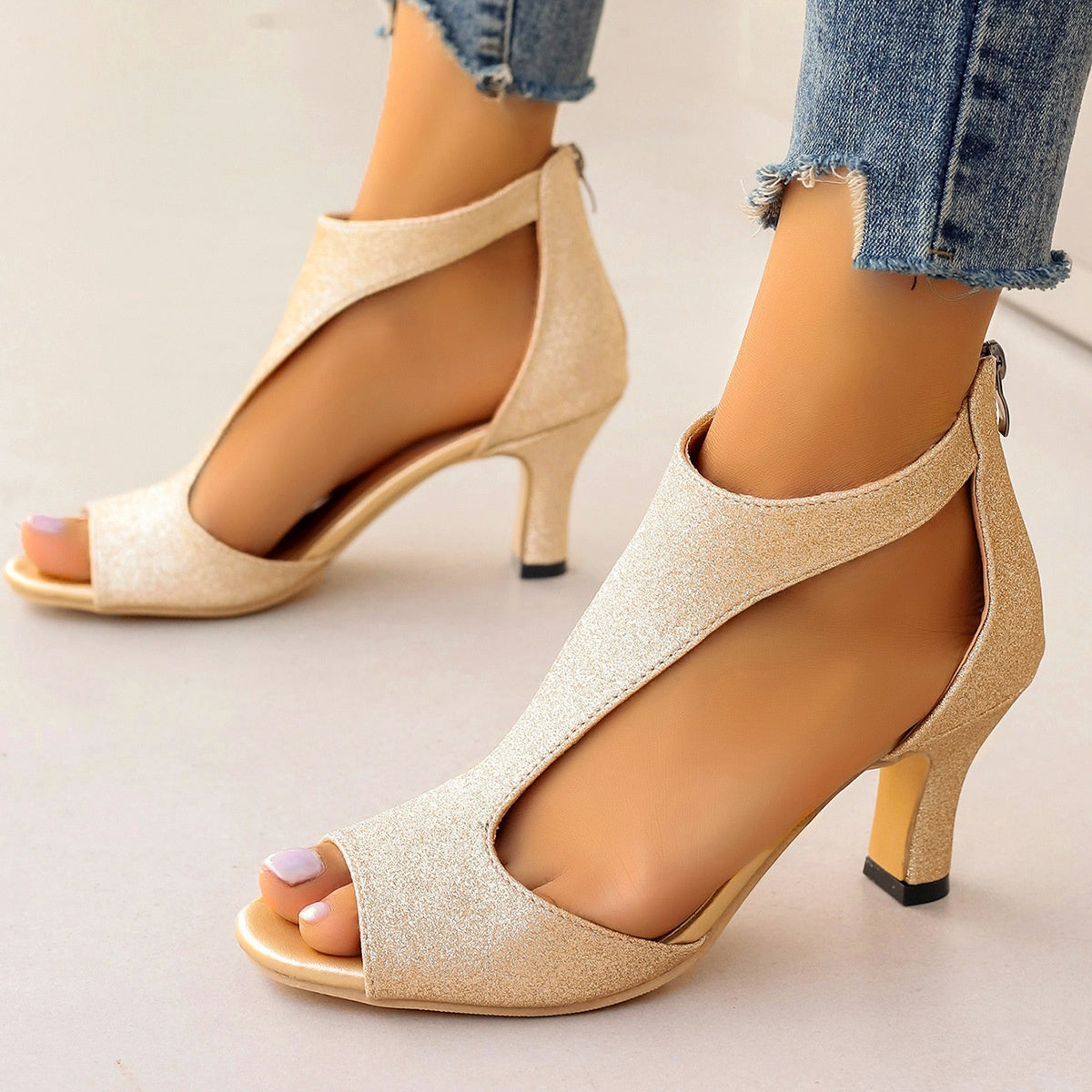 Beige high-heeled sandals worn with rolled-up jeans on a neutral background