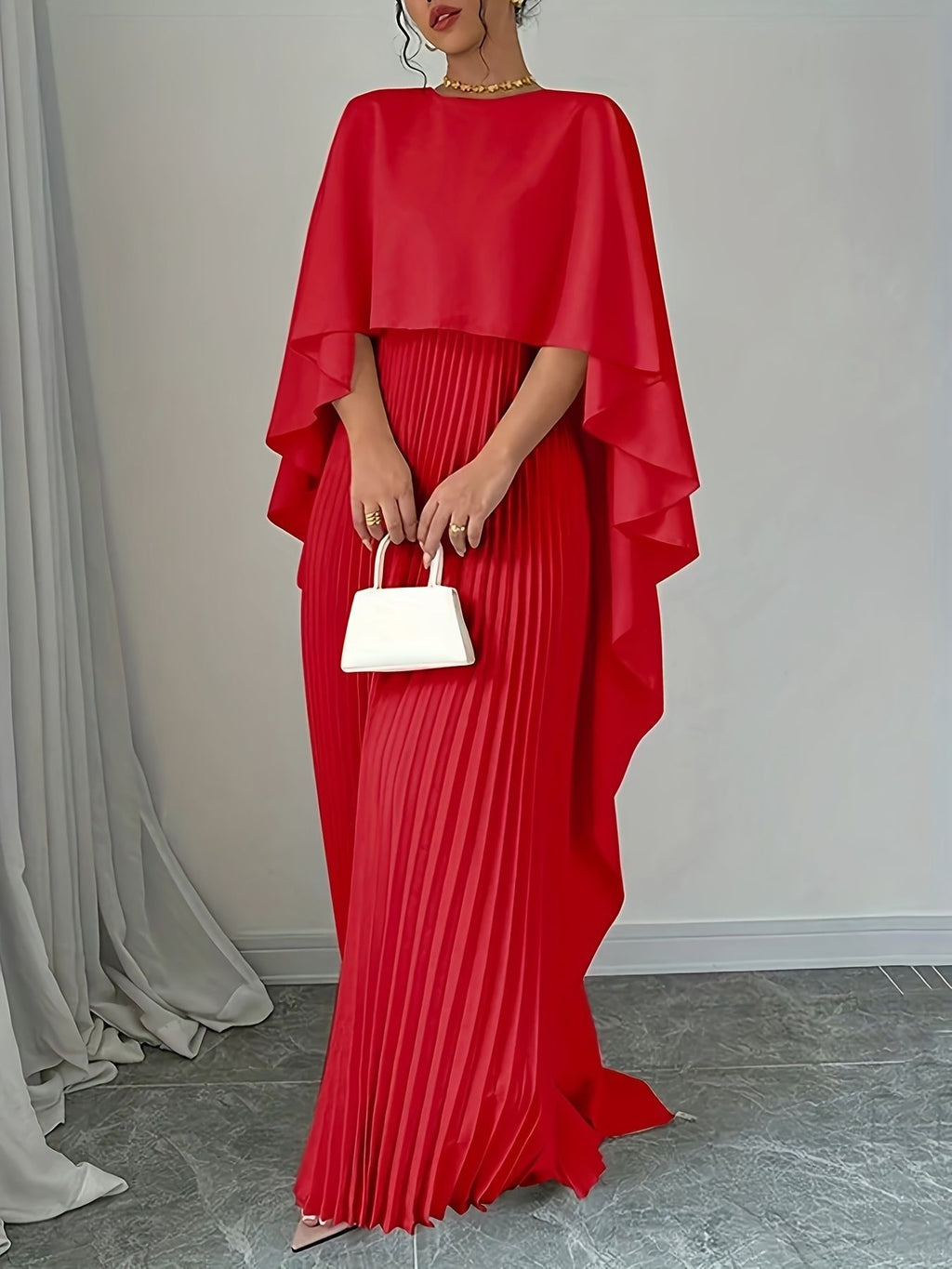 Person wearing a red dress with a cape holding a white handbag indoors.