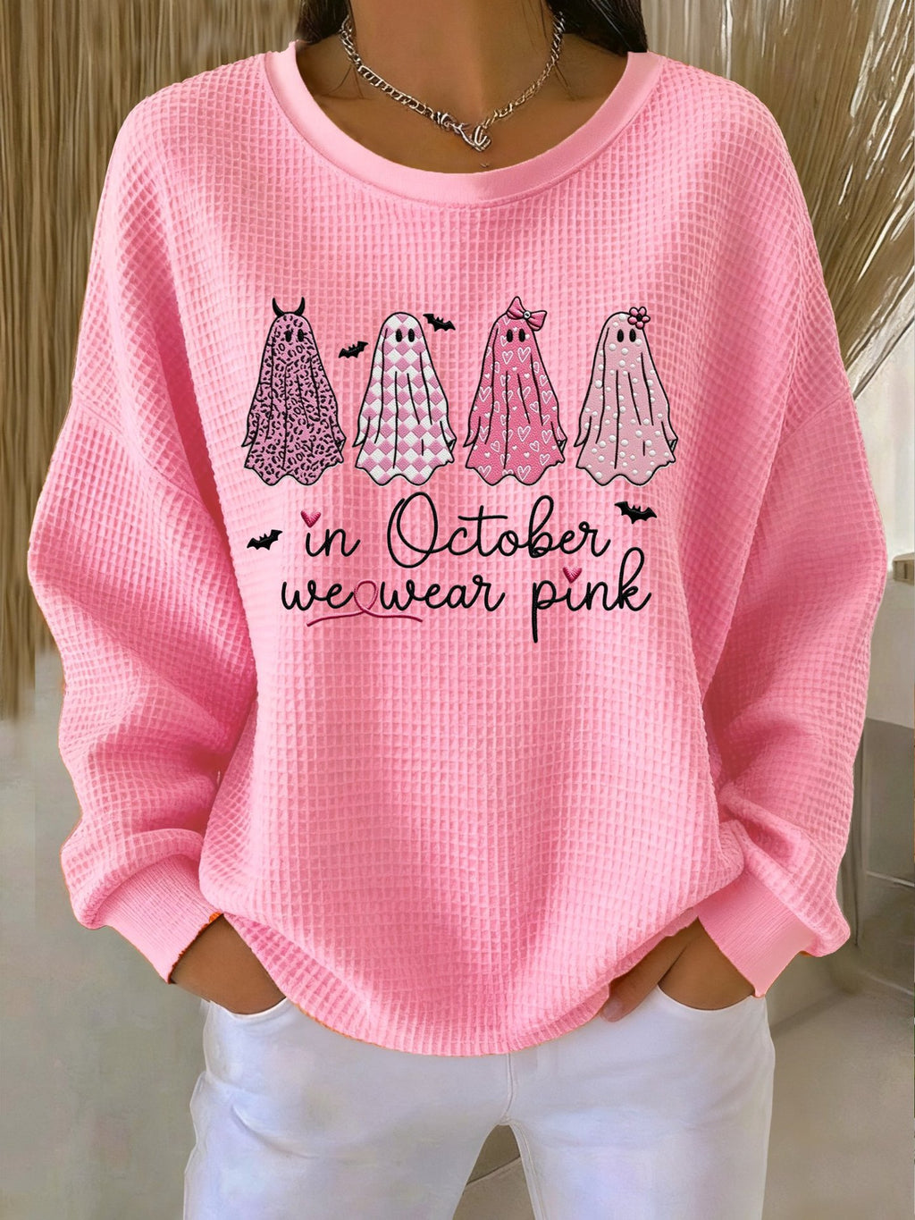 Pink sweatshirt with ghost illustrations and text 'In October we wear pink' worn by a person.