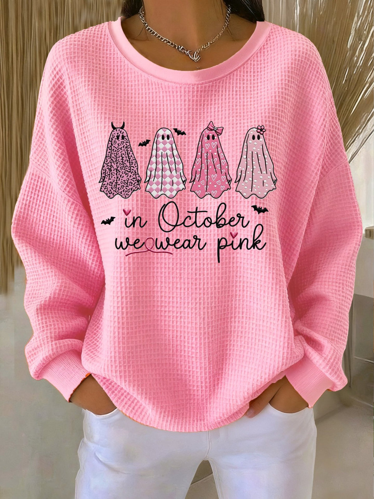 Pink sweatshirt with ghost illustrations and text 'In October we wear pink' worn by a person.