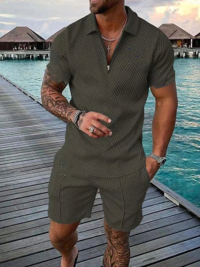 Man wearing a green patterned outfit standing on a wooden dock by water.