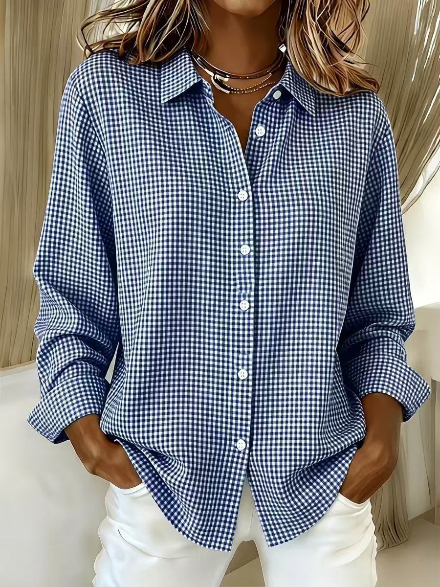 A woman wearing a blue and white gingham check long-sleeve button-up shirt with white pants, standing indoors.
