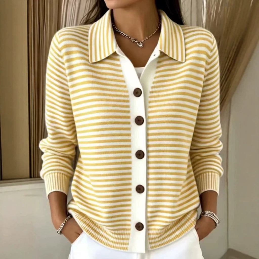 A woman wearing a yellow and white striped knit cardigan with a white placket and dark brown buttons, paired with white pants and jewelry, in an indoor setting.