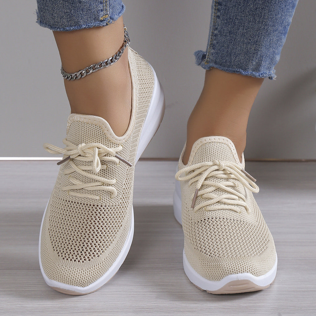 Beige sneakers with white soles worn with blue jeans on a neutral background