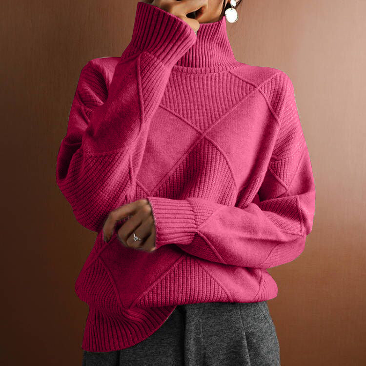 A person wearing a bright pink ribbed turtleneck sweater with a diamond-pattern knit design on the front, paired with gray bottoms, set against a warm brown background.