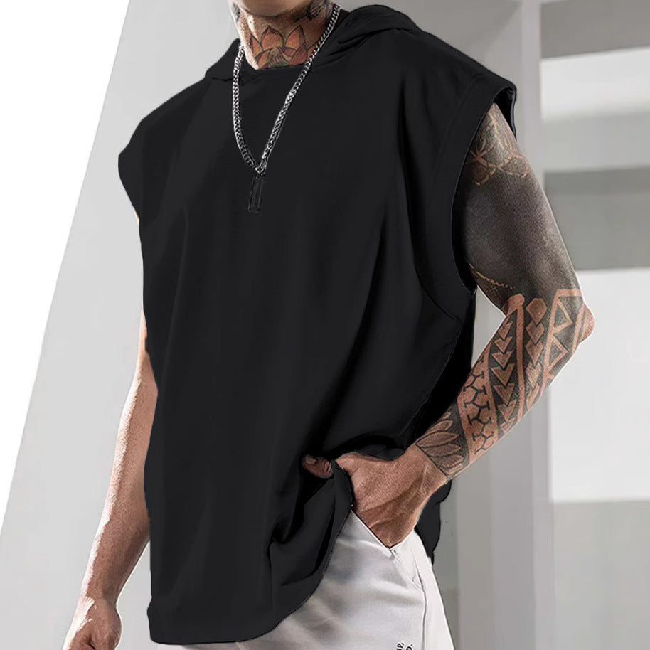 Person wearing a black sleeveless hoodie with tattoos on arms, standing against a light background.