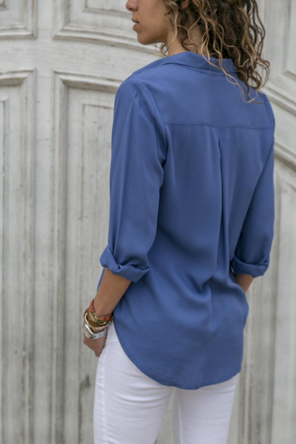Person wearing a blue shirt and white pants against a textured wall.