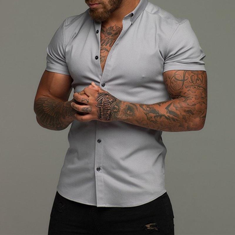 Man wearing a light gray button-up shirt with tattoos on arms against a gray background