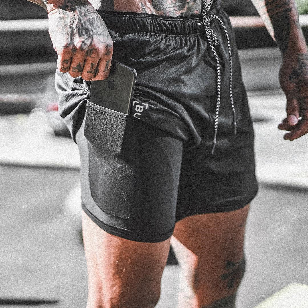 Person wearing black athletic shorts with a visible brand logo, standing on a street.
