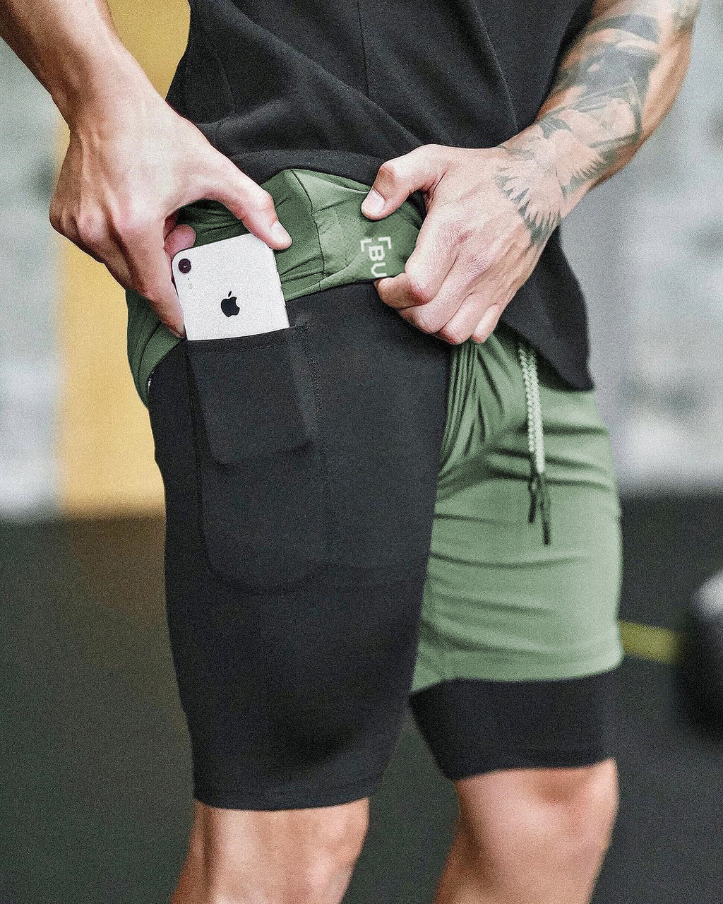 Person wearing black and green shorts with a phone in the pocket.