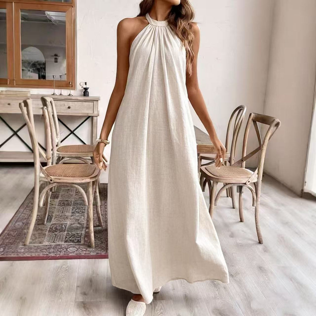 Woman in a white dress standing in a room with wooden chairs and a mirror.
