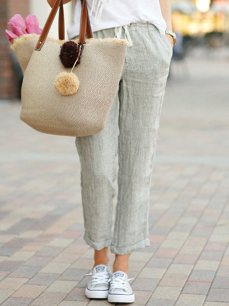 Person wearing light-colored pants and white sneakers, holding a beige tote bag with pom-poms.