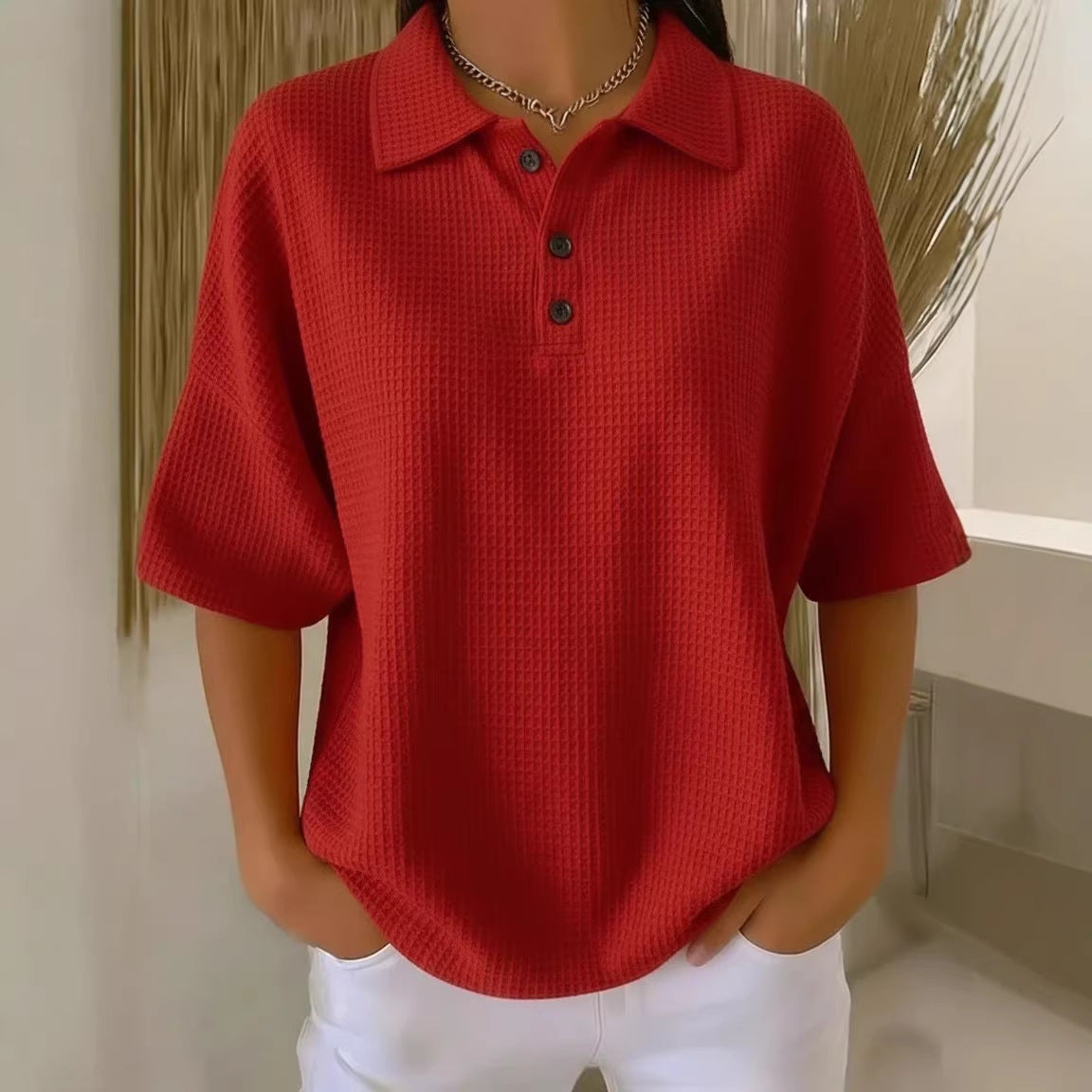 Person wearing a red textured polo shirt with black buttons indoors.