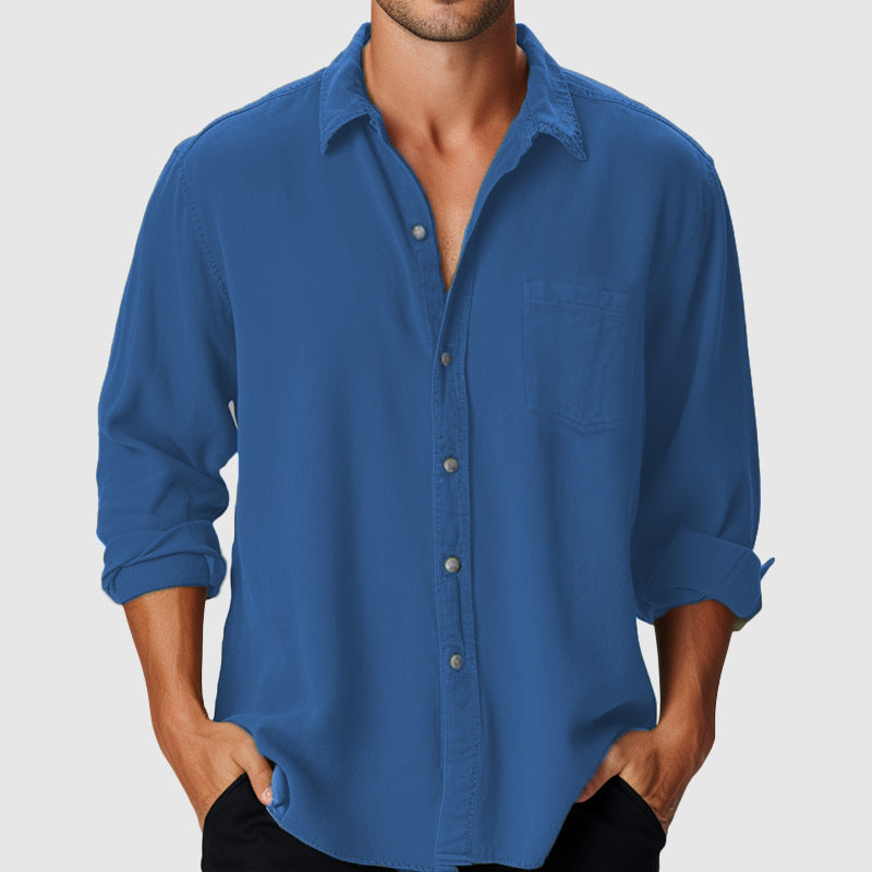 Man wearing a blue button-up shirt with rolled-up sleeves on a gray background