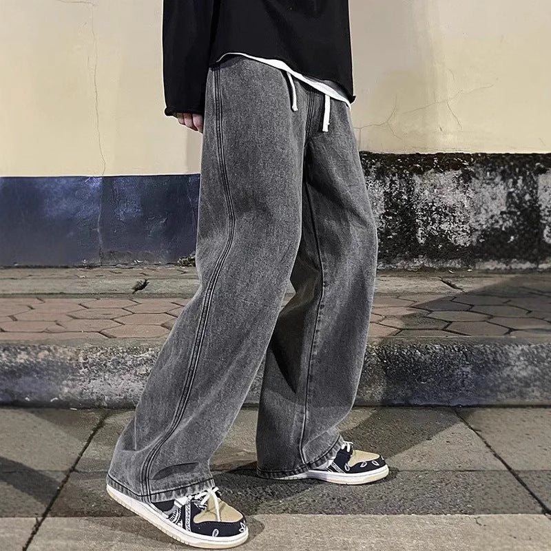 Person wearing gray jeans and black shoes standing on a sidewalk.