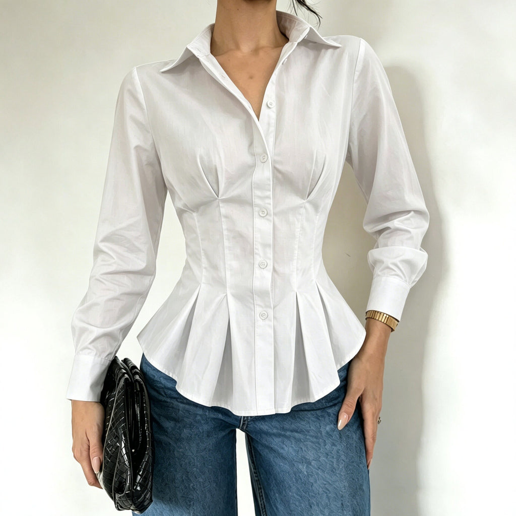 A woman wearing a fitted white long-sleeve button-up blouse with a peplum hem and structured shoulders, paired with blue jeans and holding a black clutch against a plain light background.