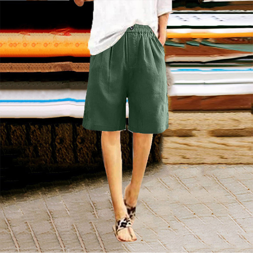 Person wearing green shorts standing on a stone pavement with a stack of colorful fabrics in the background.
