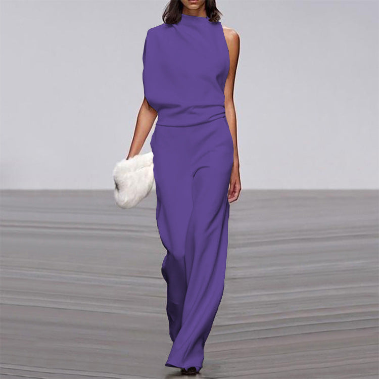 Woman wearing a purple jumpsuit holding a white fur bag on a gray floor.