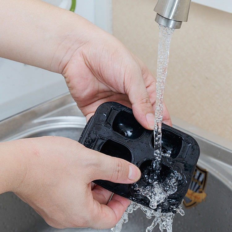Person washing a black ice cube tray under running water from a faucet.