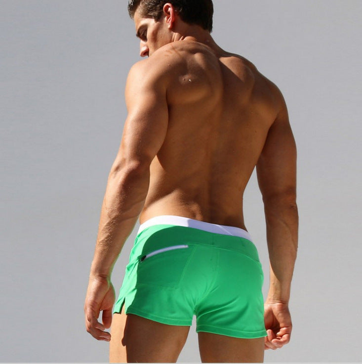 Man wearing green swim shorts with a white waistband on a gray background