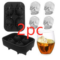 Two black skull-shaped ice cube trays with a glass of whiskey and ice cubes.