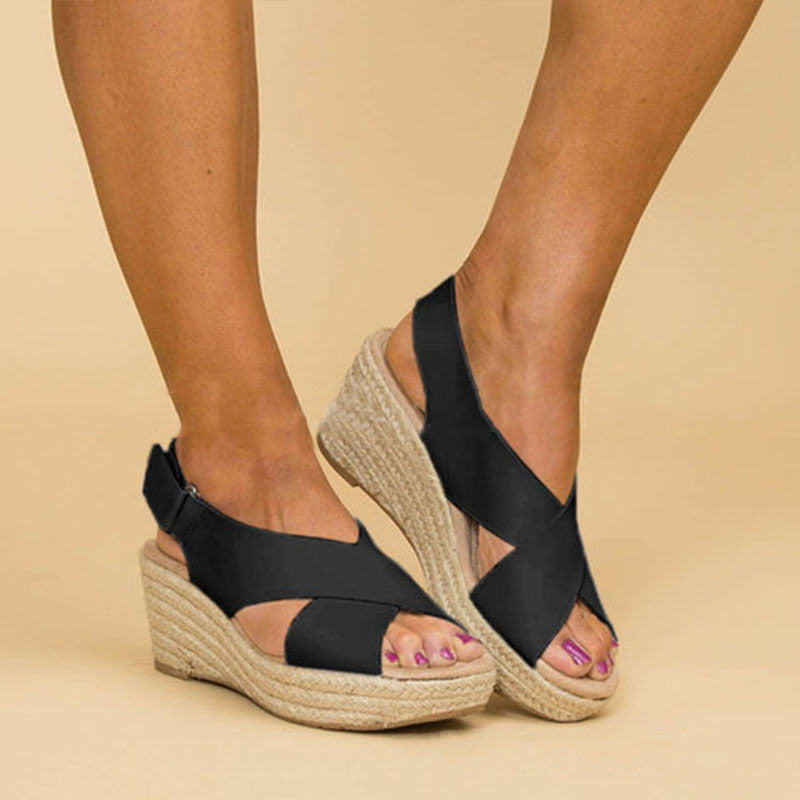 Black wedge sandals with espadrille sole worn by a person on a beige background
