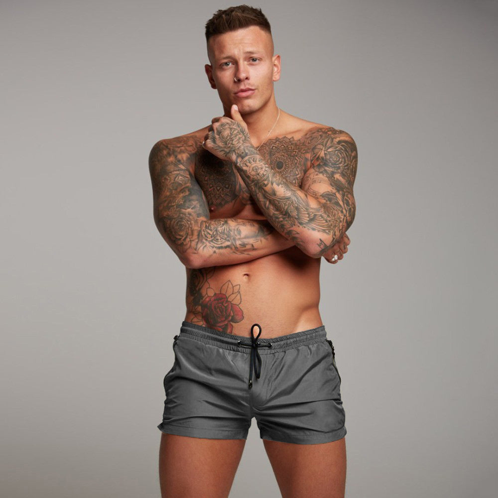 Man with tattoos wearing gray shorts against a gray background