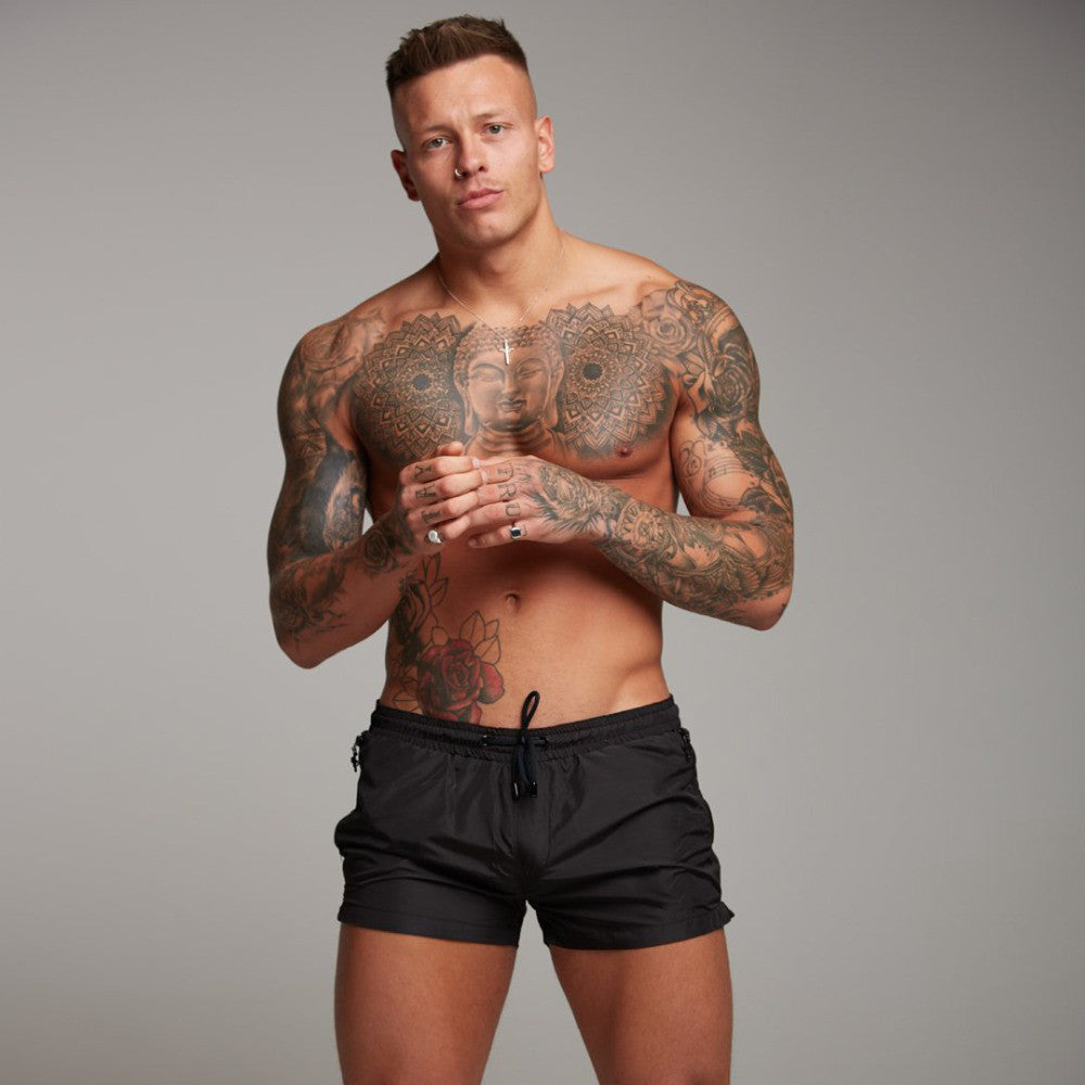 Man with tattoos wearing black shorts against a gray background