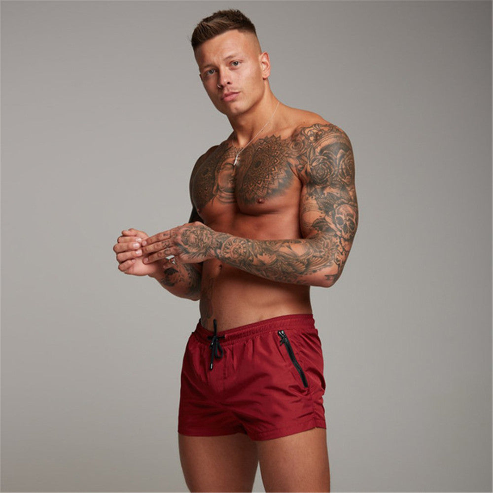 Man with tattoos wearing red shorts against a gray background