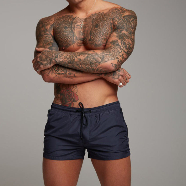 Man with tattoos wearing navy swim shorts against a gray background